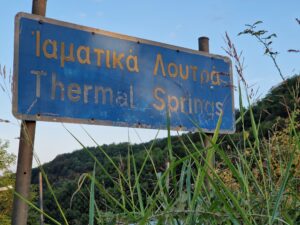 Town entrance sign saying "Ίαματικά Λουτρά - Thermal Springs"